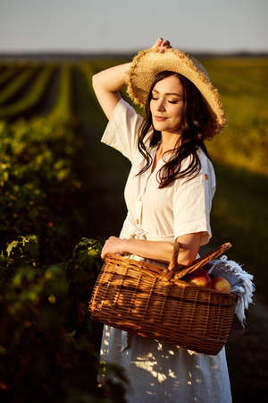 Girl in straw hat holding picnic basket with fruits.の写真素材