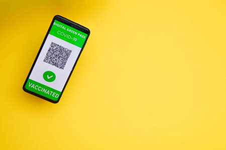 Greenpass digital covid certificate vaccinated with dummy QR code, on a yellow background.Copy spaceの写真素材