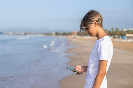 Close up handsome smiling teenager boy using smartphone at the beach on summer holidays.の写真素材