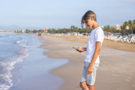 Handsome smiling teenager boy using smartphone at the beach on summer weekend vacation.の写真素材