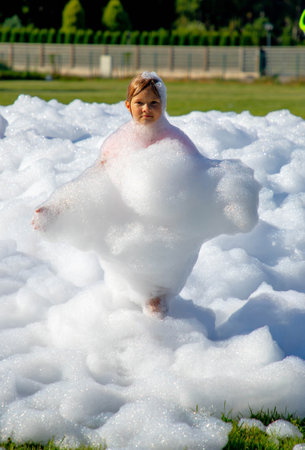 Child girl playing in foam outdoors on sunny day at foam partyの写真素材