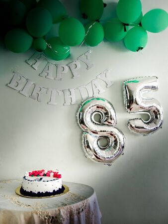 cake to celebrate an 85th birthday with green balloons and a light that illuminates the cakeの写真素材
