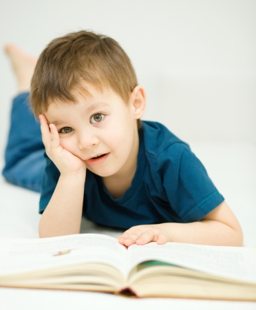 Cute little boy is reading book while sitting at table, indoor shootの写真素材