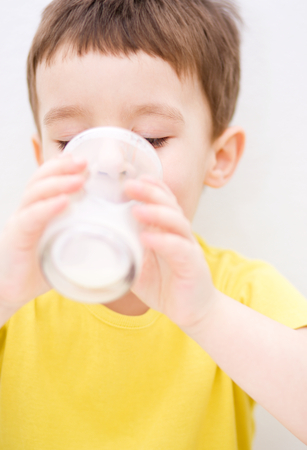 Cute little boy is dipping his tongue in the glass of milkの写真素材