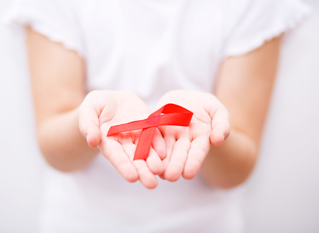 Healthcare and medicine concept - girl hands holding red breast cancer awareness ribbonの写真素材