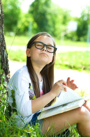 Cute little girl is reading a book outdoorsの写真素材