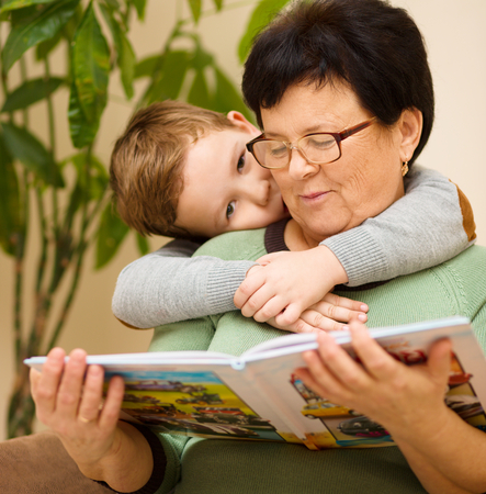 Grandmother is reading book with her grandson, indoorsの写真素材
