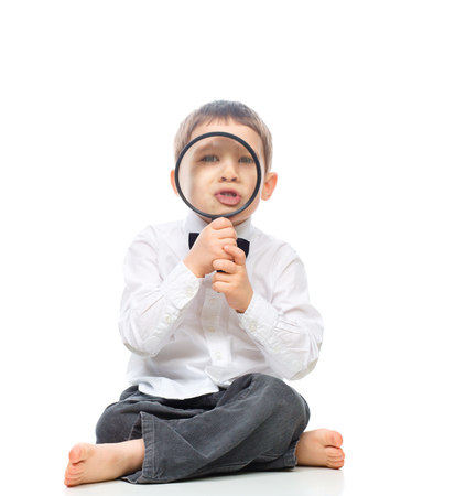 Cute little boy is looking through magnifier, isolated over whiteの写真素材