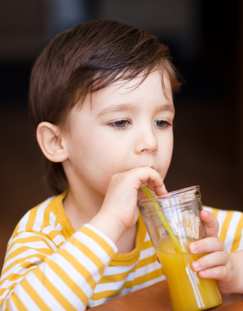 Little boy is drinking orange juice using strawの写真素材