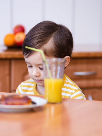 Little boy is drinking orange juice using strawの写真素材