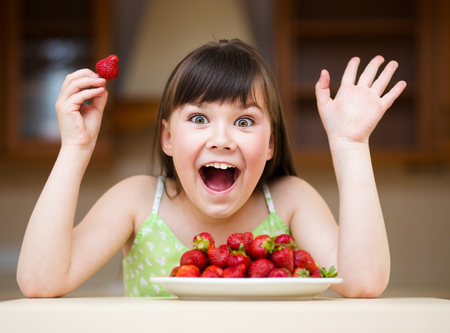 Happy little girl eats strawberriesの写真素材