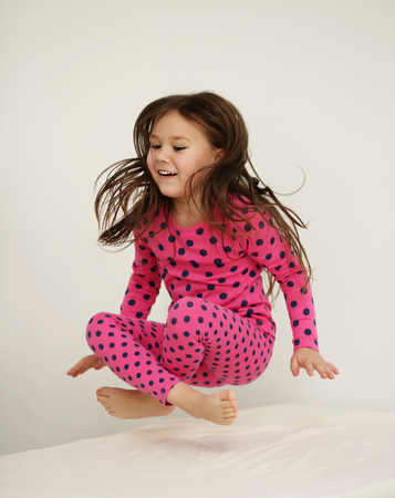Cute happy girl jumping on the bed at homeの写真素材