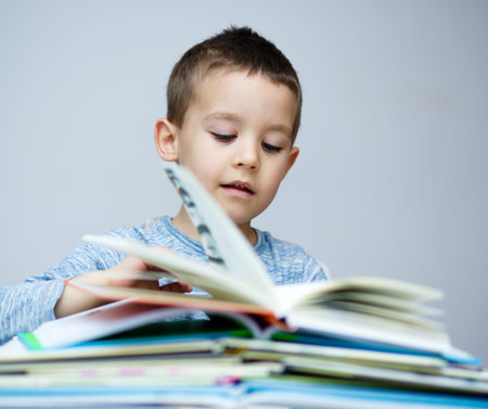 Cute little boy is reading book while sitting at table