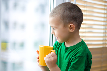 Cute boy is drinking tea sitting at the windowの写真素材