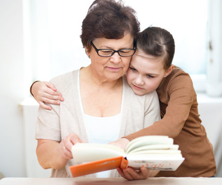Grandmother is reading book with her granddaughter, indoorsの写真素材