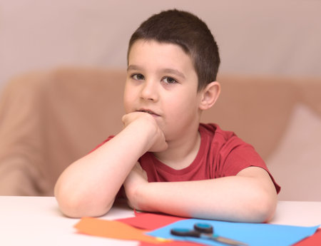 Cute smiling boy is cutting paper using scissors. Education, school concept