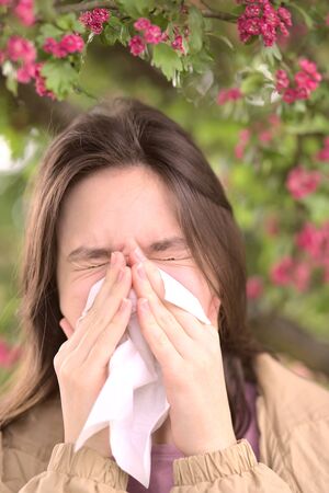 Young girl is blowing her nose near spring tree in bloom. Health and medicine conceptの写真素材