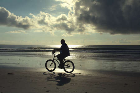 Silhouette of man riding bike on the beach.の素材
