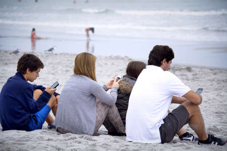 Texting on mobiles phone on the beach.の素材