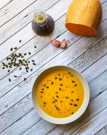 Pumpkin cream on white wooden table with pumpkin seeds and olive oilの写真素材