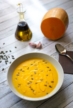 Pumpkin cream on white wooden table with pumpkin seeds and olive oilの写真素材