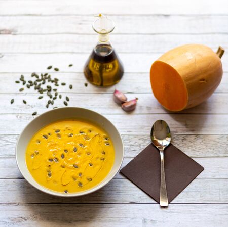 Pumpkin cream on white wooden table with pumpkin seeds and olive oilの写真素材