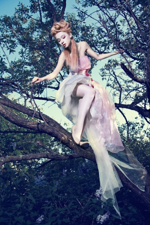 Lovely young lady wearing elegant white dress with roses standing on the tree in woodの写真素材