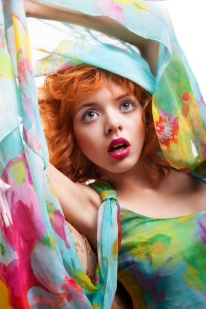 Girl with beautiful red hair and colorful dress and fabric over white backgroundの写真素材