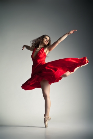 Gorgeous young ballet dancer wearing red dress over dark grey backgroundの写真素材