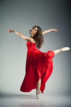 Gorgeous young ballet dancer wearing red dress over dark grey backgroundの写真素材