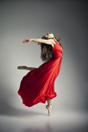 Gorgeous young ballet dancer wearing red dress over dark grey backgroundの写真素材