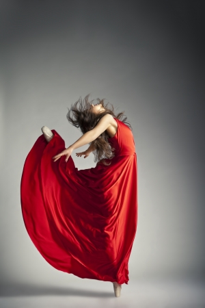 Gorgeous young ballet dancer wearing red dress over dark grey backgroundの写真素材