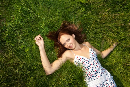 Woman relaxing outdoors looking happy and smiling on green grassの写真素材