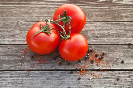Dewy red tomatoes with pepper on old wooden tableの写真素材