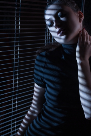 Sexy woman in black dress with jalousie looking through the window with jalousieの写真素材