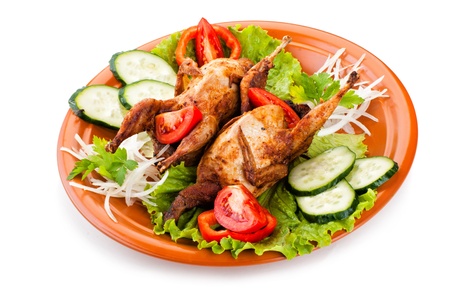 Two fresh grilled whole quail with cucumber, raw tomatoes and onion on plate with leaf lettuce isolated over white backgroundの写真素材