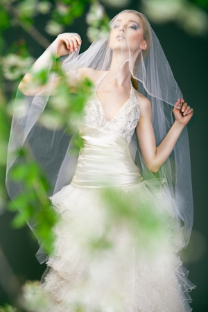 Portrait of a woman in wedding dress behind the green branches with flowersの写真素材
