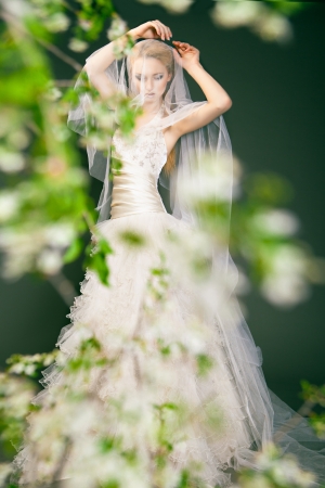 Portrait of a woman in wedding dress behind the green branches with flowersの写真素材