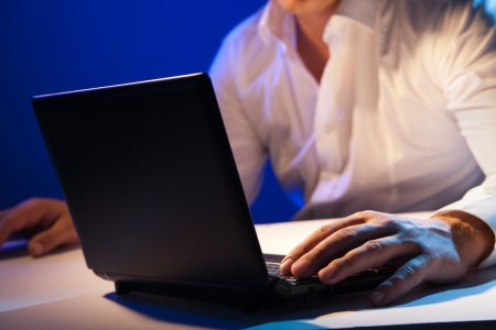 Close up of young businessman working on a laptop on dark backgroundの写真素材