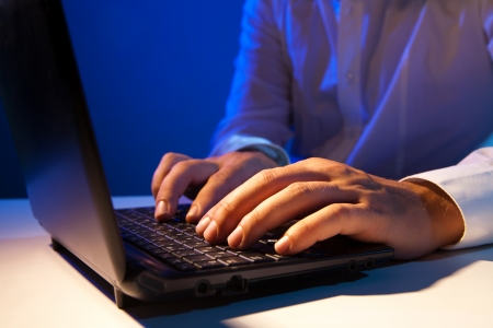 Close up of young businessman working on a laptop on dark backgroundの写真素材