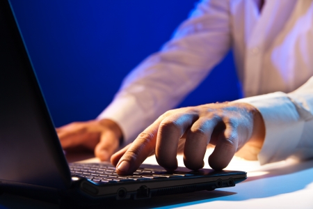 Close up of young businessman working on a laptop on dark backgroundの写真素材