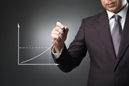 Business man drawing a growing graph on the screen over dark backgroundの写真素材