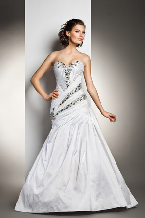 The beautiful young woman posing in a wedding dress over grey backroundの写真素材