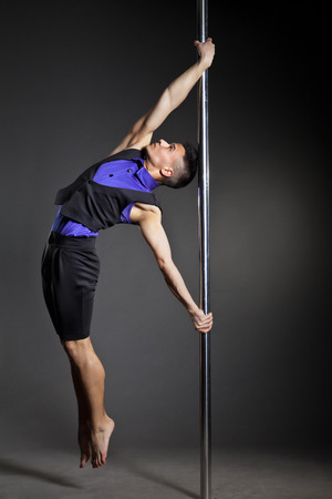 Young strong pole dance man over black background with flashesの写真素材