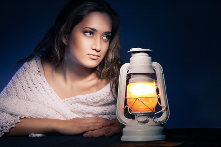 portrait of beautiful woman sitting with lantern over dark backgroundの写真素材
