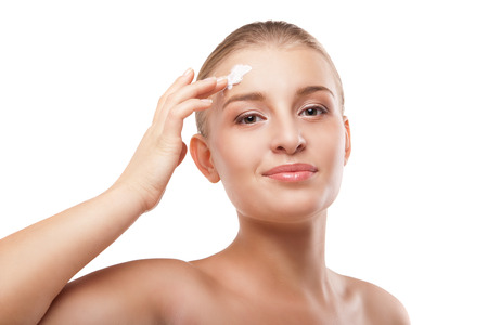 Portrait of young woman applying moisturizer cream on clean fresh face isolatedの写真素材
