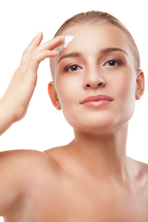 Portrait of young woman applying moisturizer cream on clean fresh face isolatedの写真素材
