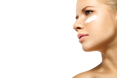 Portrait of young woman applying moisturizer cream on clean fresh face isolatedの写真素材