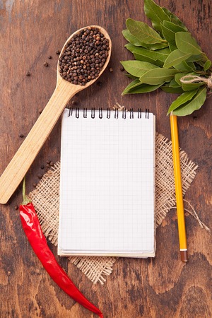 Red chili pepper, garlic, bay leaf, spices in spoons, old notebook on oak wood texture background. Spicesの写真素材