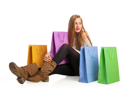 Beautiful excited woman sitting among colorful shopping bagsの写真素材